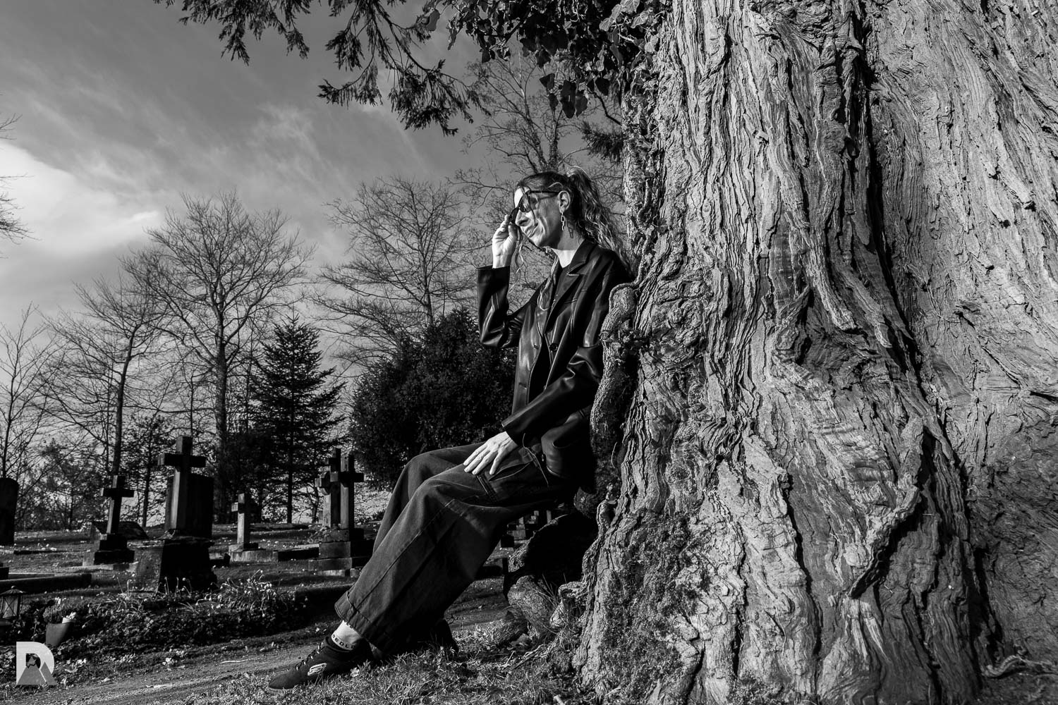 s/w: Sitzend auf der Zederwurzel. Das Holz der Zeder mit der maserigen groben Musterung passt gut zu den grauen Grabsteinen im Hinergrund